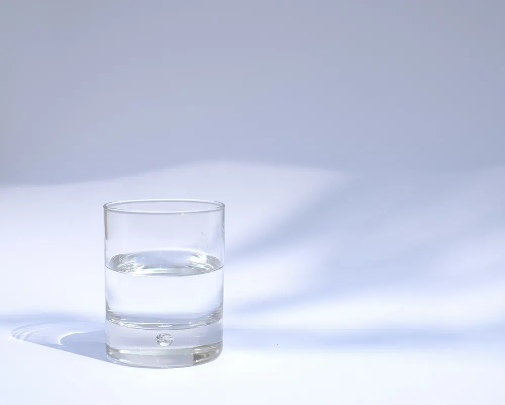 A half-full glass of clear water on a white surface in soft light